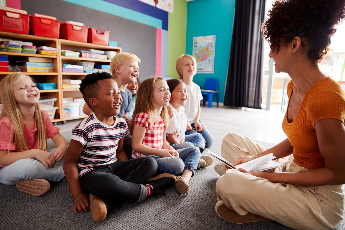 Teacher sitting on the floor reading a story to a group of young pupils