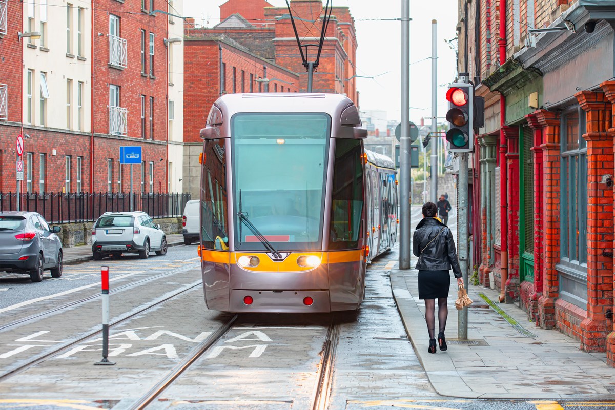 Luas tram on a red-brick street in Dublin with a woman walking on the pavement