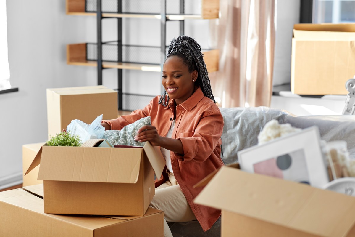 Smiling woman unpacking a cardboard box on a sofa in a new home