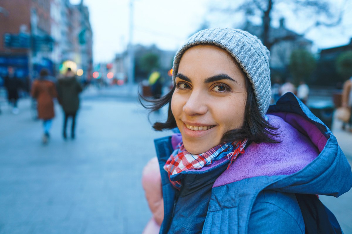 Smiling woman in a knitted hat turning to the camera on a busy city street at dusk