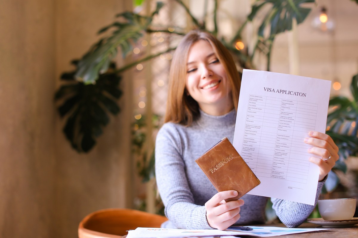 Woman at a cafe table looking at a visa application form and holding a passport