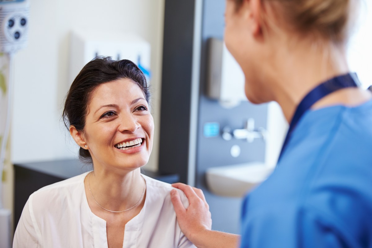Smiling woman patient talking with a nurse in blue scrubs in a clinic room