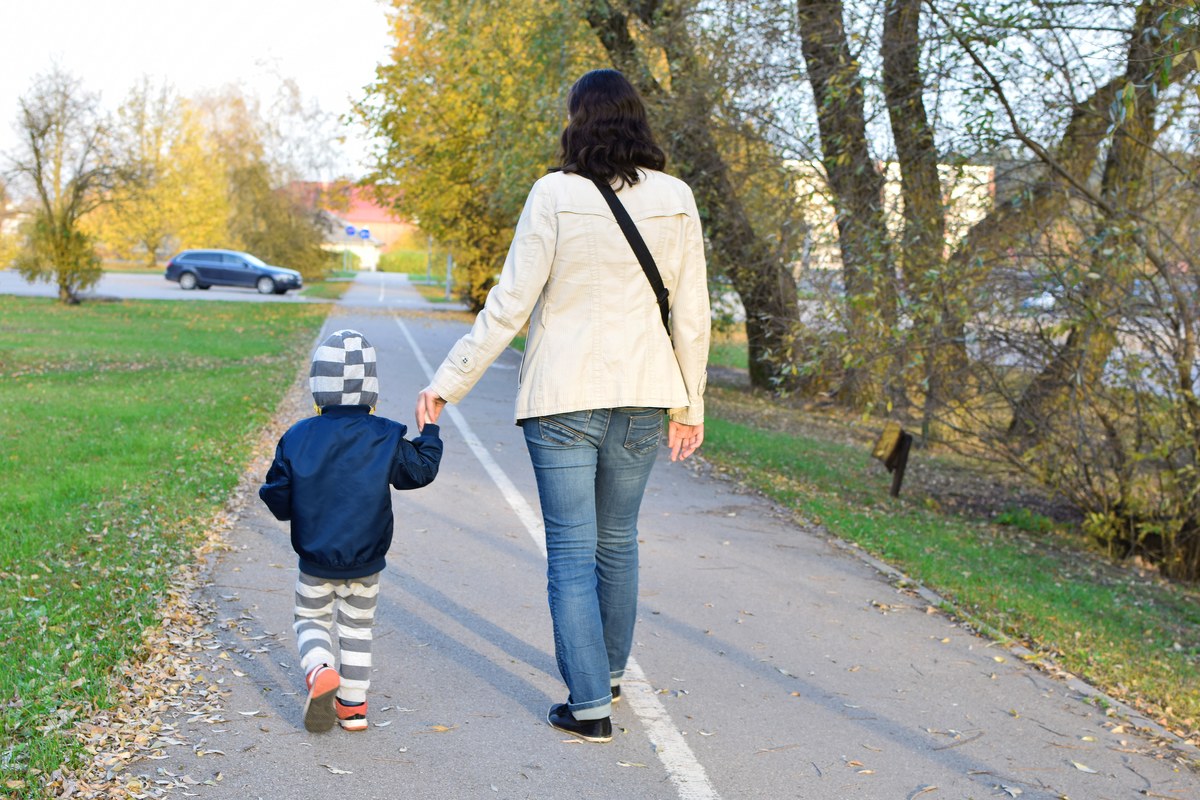Mother and small child walking hand in hand along a path under autumn trees