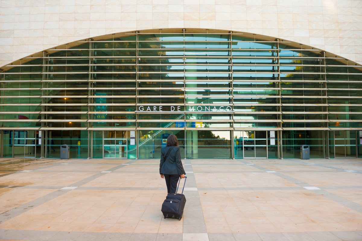 Woman pulling a suitcase towards the glass facade of Monaco railway station