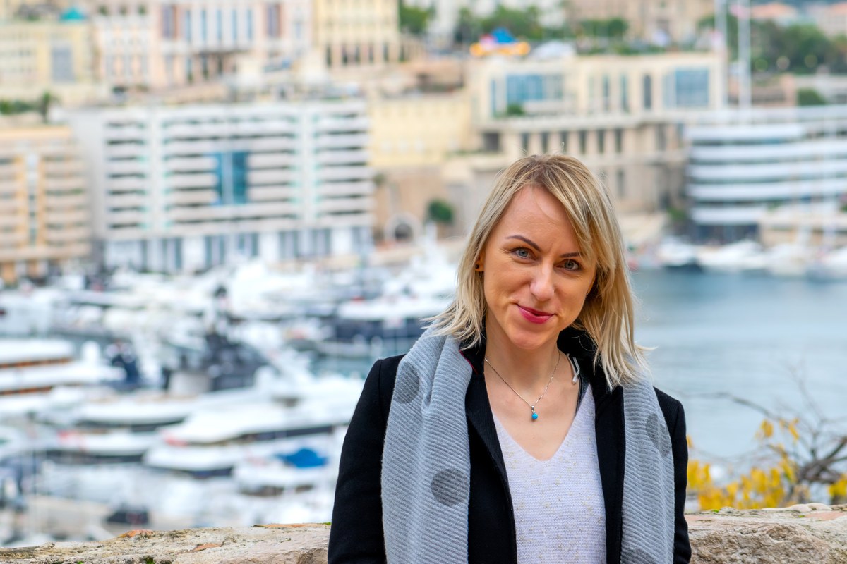 Woman with a grey scarf in front of Monaco harbour and apartment buildings