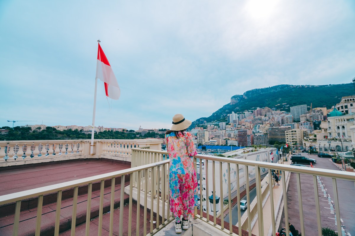 Woman on a terrace beside the red and white flag of Monaco above the harbour