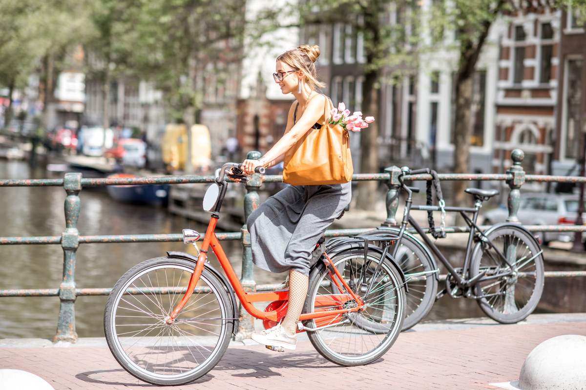 Woman cycling over a canal bridge past parked bikes and brick houses in Amsterdam
