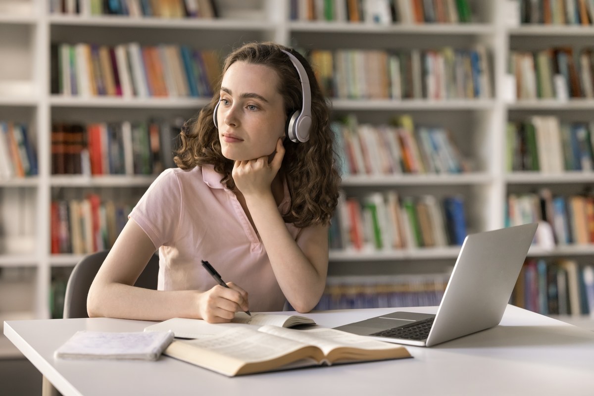 Young woman with headphones studying with a book and laptop in a library
