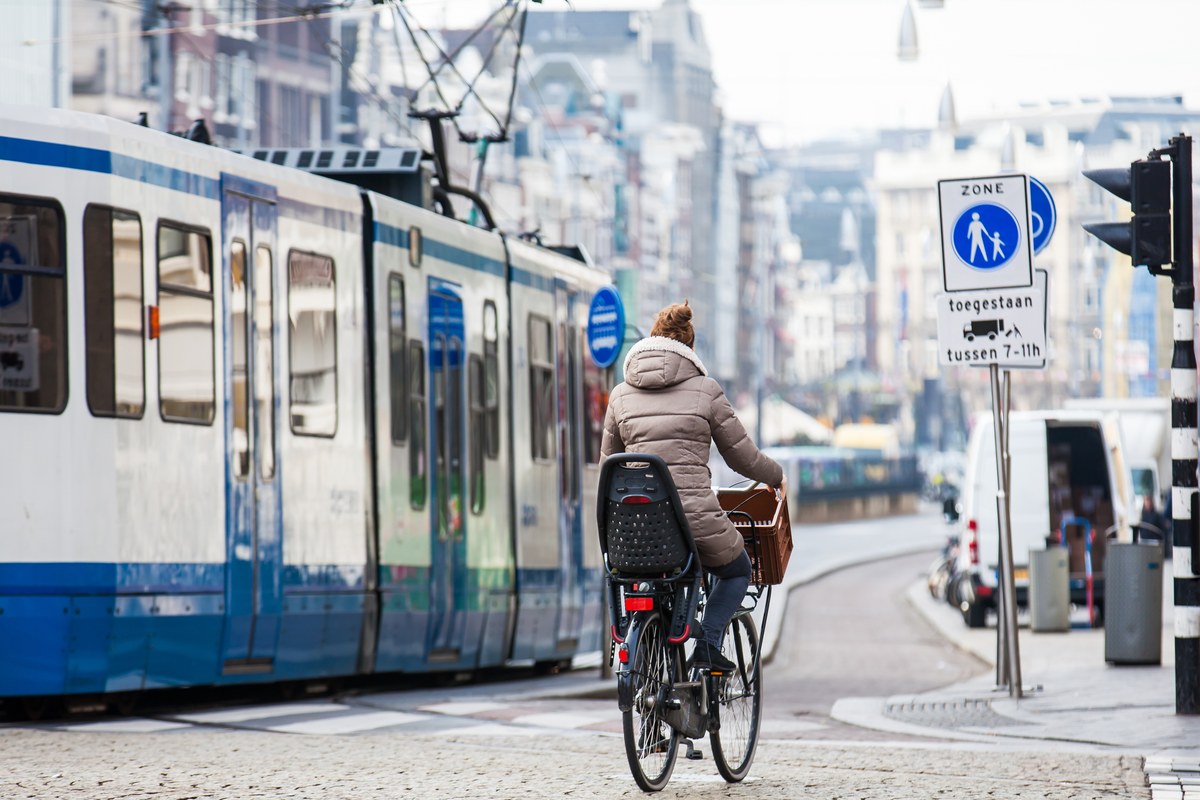 Woman cycling with a child seat beside a blue and white tram in Amsterdam