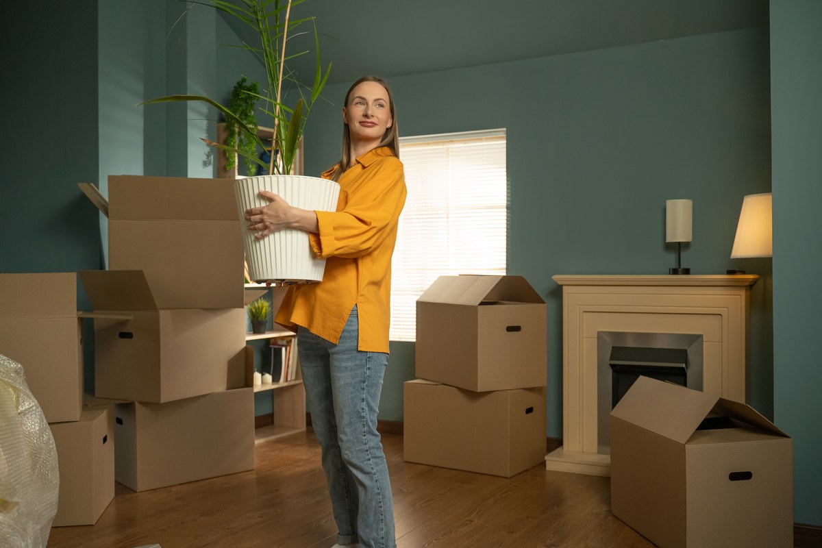 Woman carrying a potted plant among cardboard boxes in a new apartment