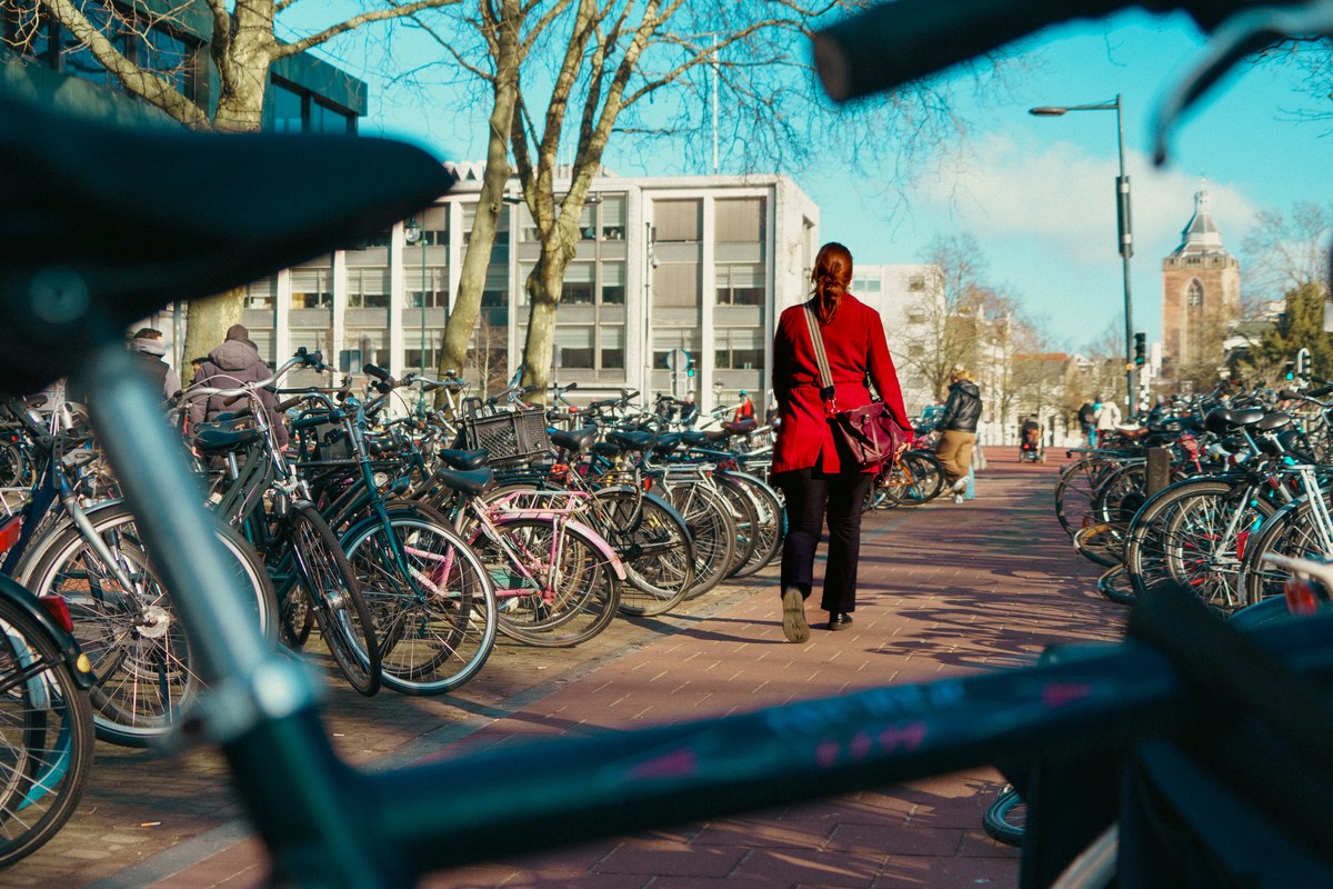 Woman in a red coat walking through a crowded bicycle parking area under bare trees