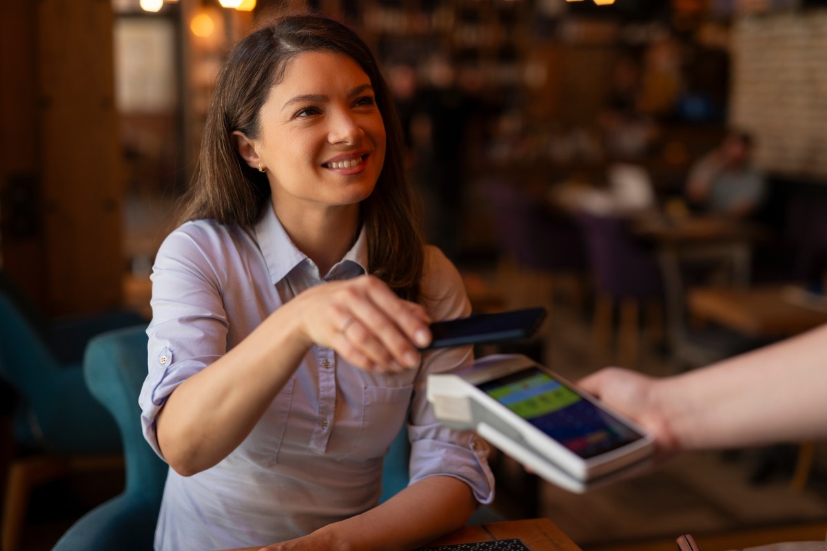 Smiling woman paying contactless with her phone at a cafe card terminal