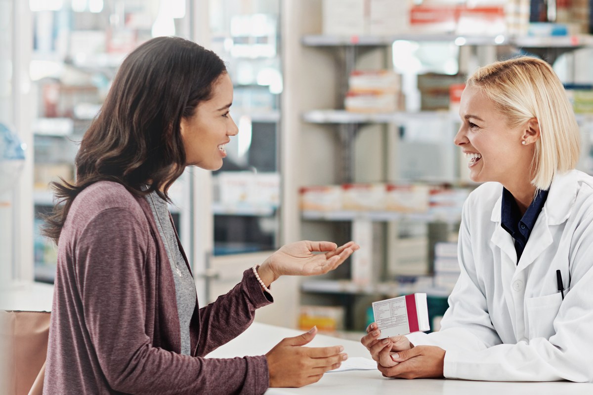 Woman talking with a pharmacist holding a medicine box at a pharmacy counter