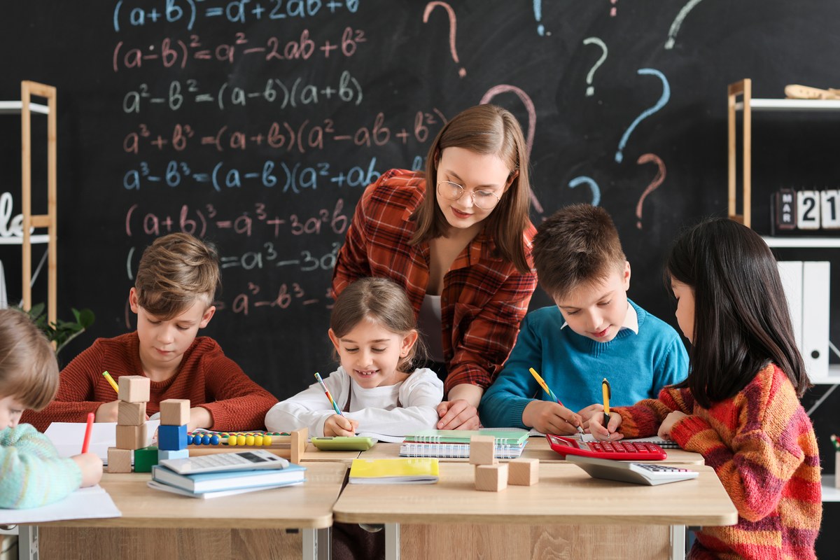 Teacher helping pupils at their desks in front of a chalkboard