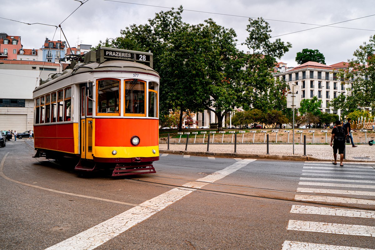 Yellow and red tram 28 to Prazeres crossing a street in Lisbon