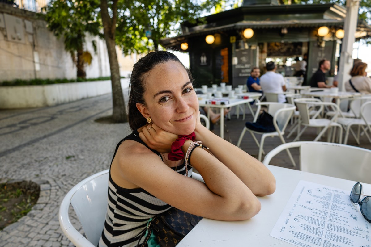 Woman resting her chin on her hands at an outdoor café table on a cobbled street