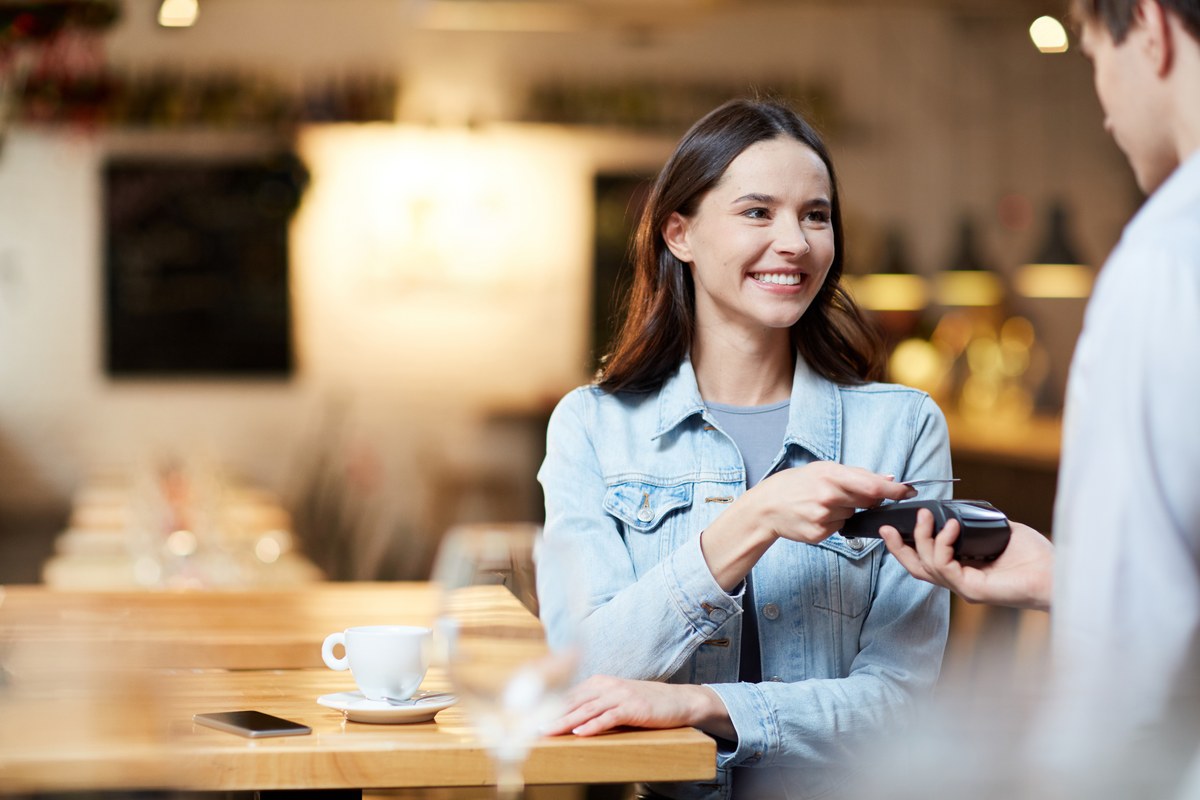 Smiling woman paying by card on a terminal at a café table