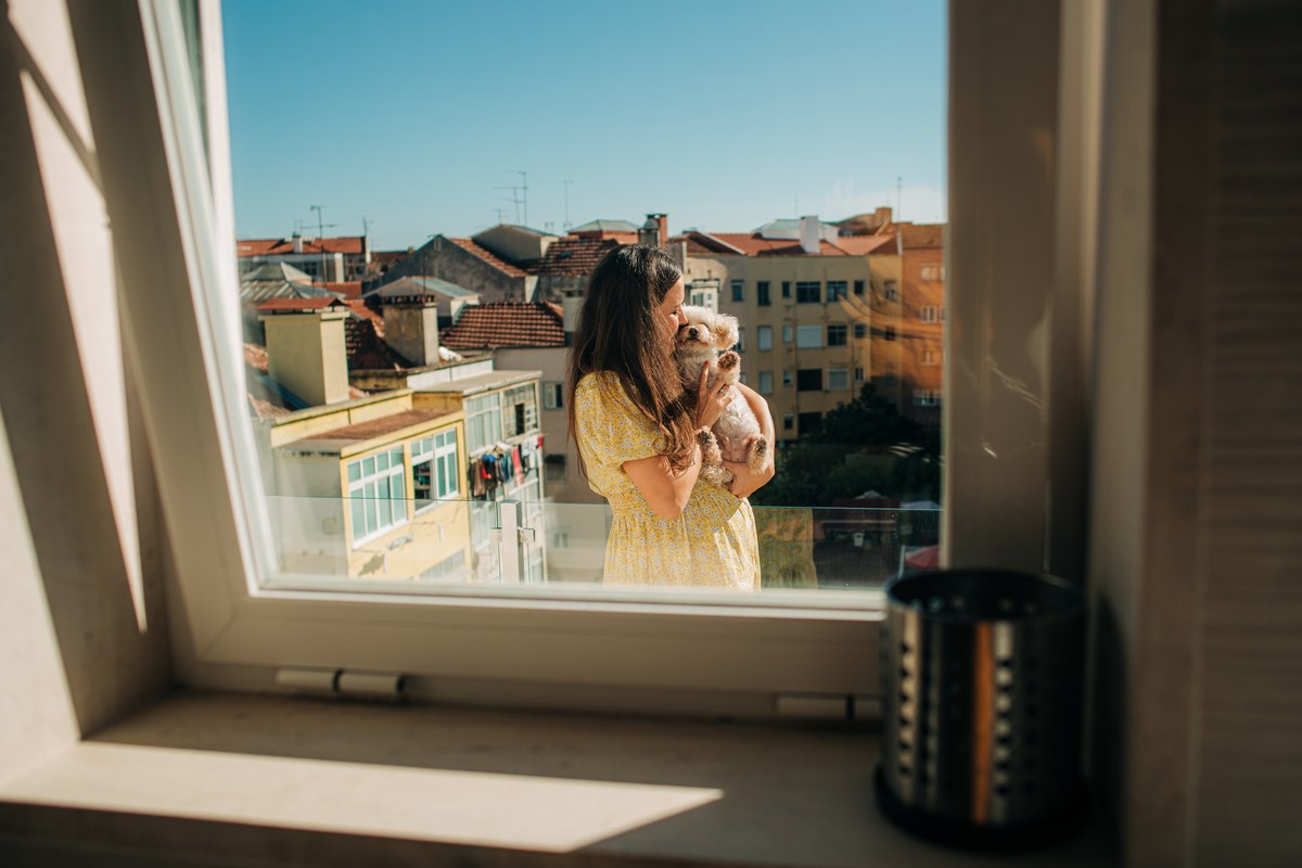 Woman holding a small dog on a balcony above the rooftops of Lisbon