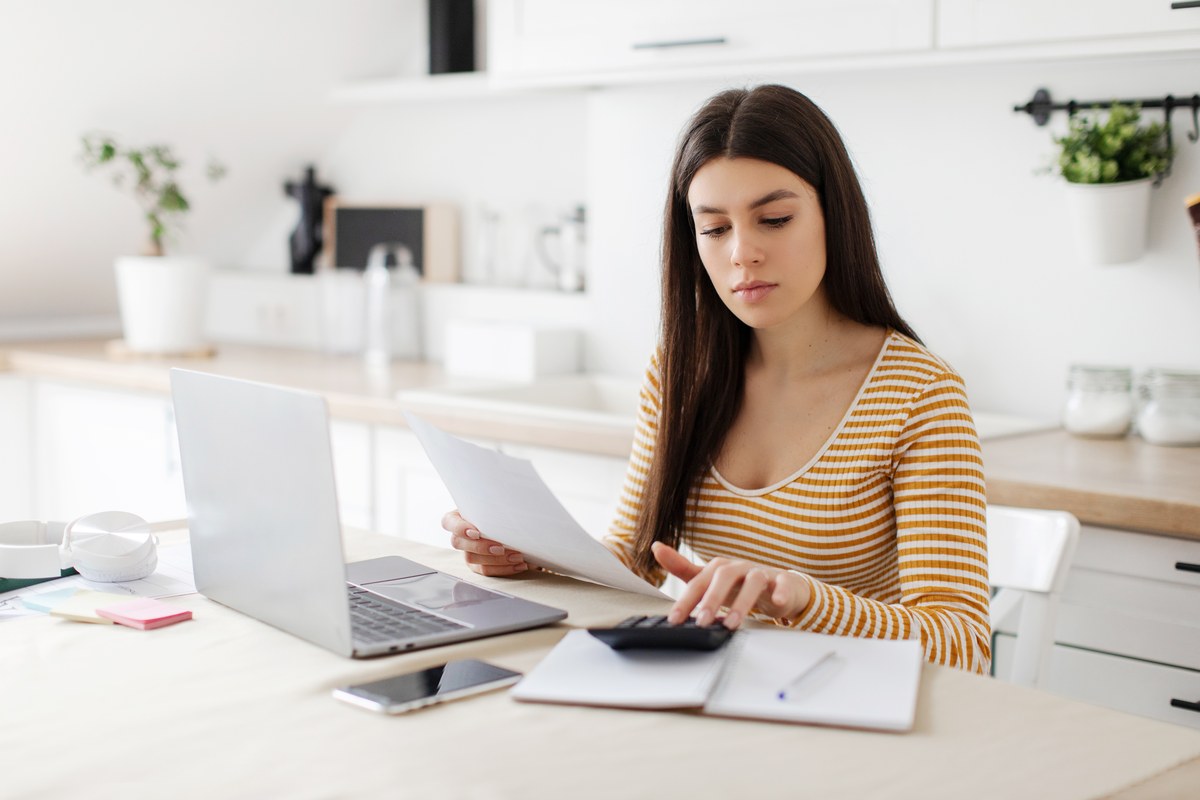 Woman with papers, laptop and calculator at a kitchen table