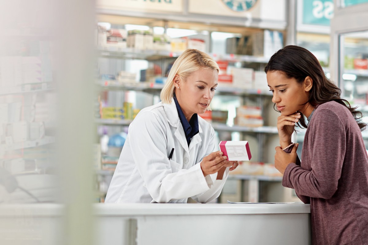 Pharmacist showing a medicine box to a woman customer at the counter
