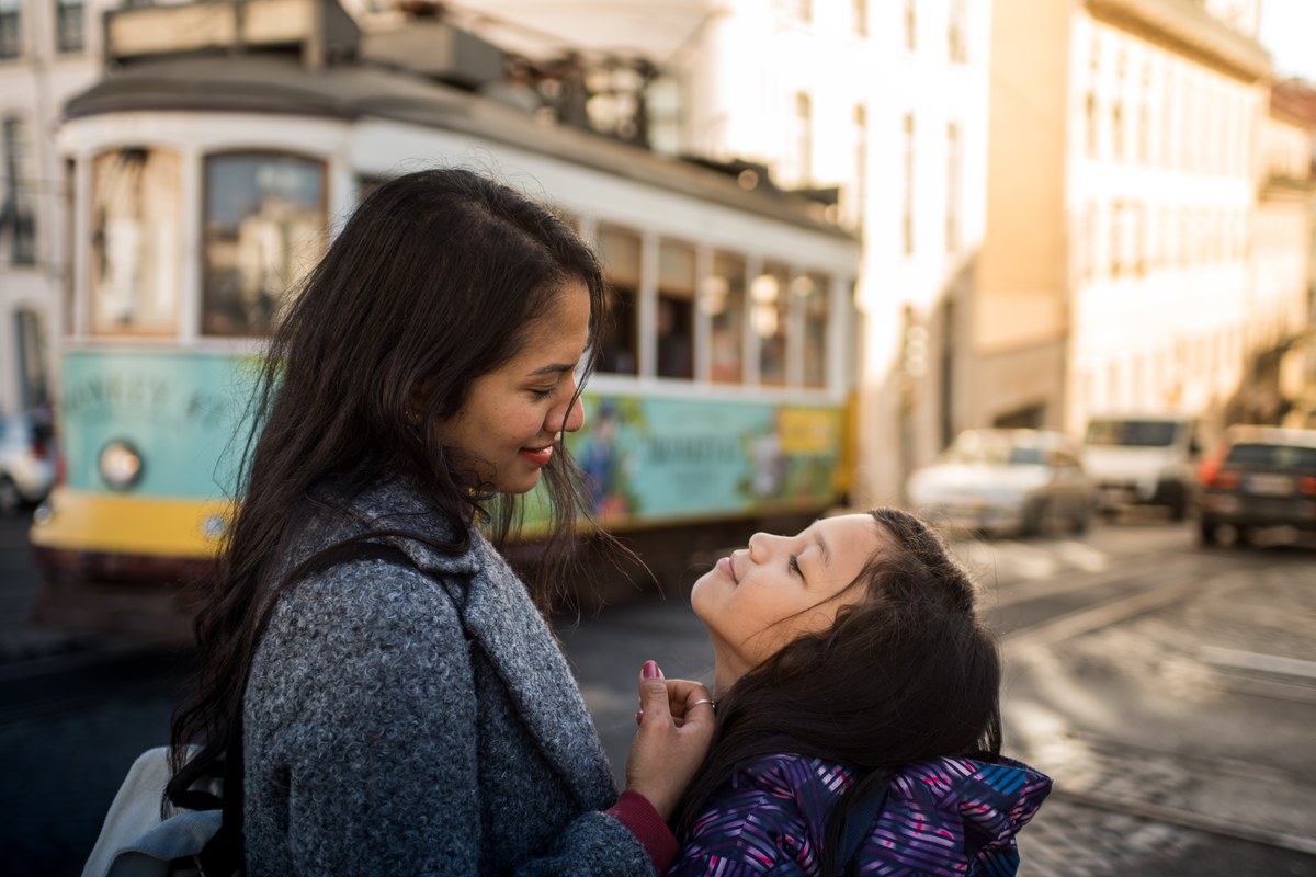 Mother and daughter face to face on a Lisbon street with a tram behind